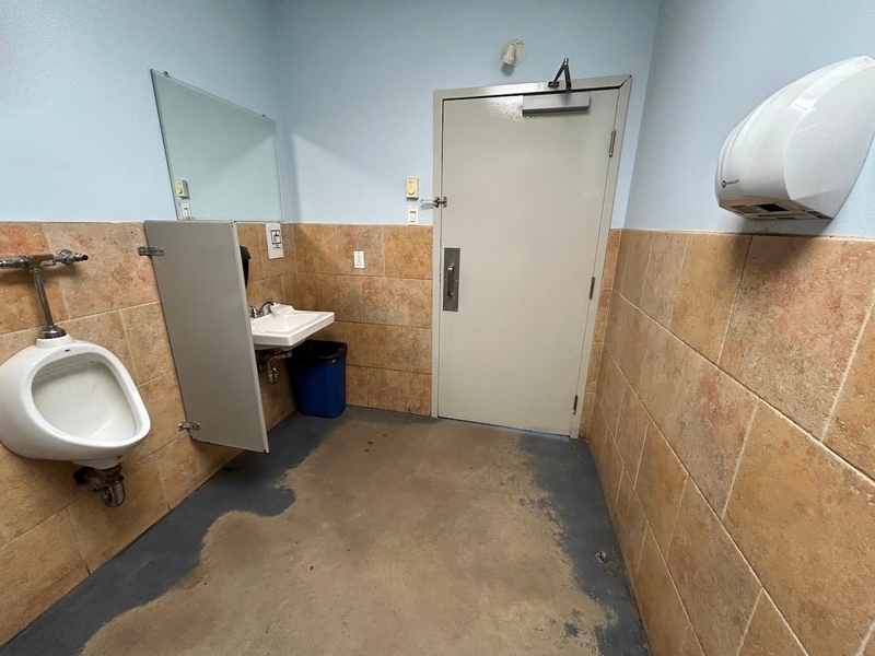 Vue sur le lavabo, l'urinoir et la porte de la salle de toilette homme