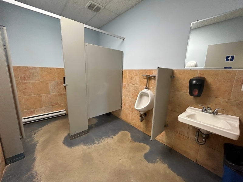 Vue sur le cabinet de toilette, l'urinoir et le lavabo de la salle de toilette homme